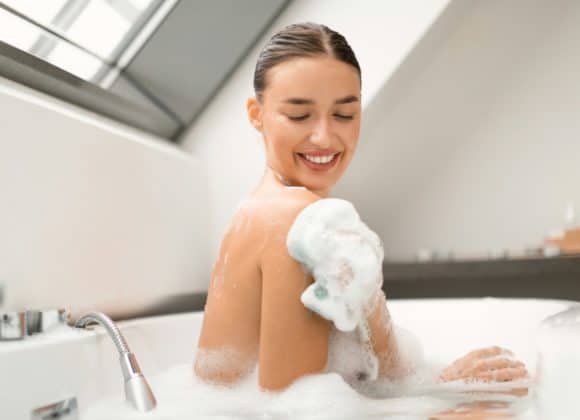 Happy Female Rubbing Body With Sponge Taking Bath At Home