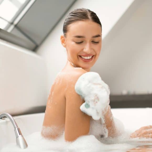 Happy Female Rubbing Body With Sponge Taking Bath At Home