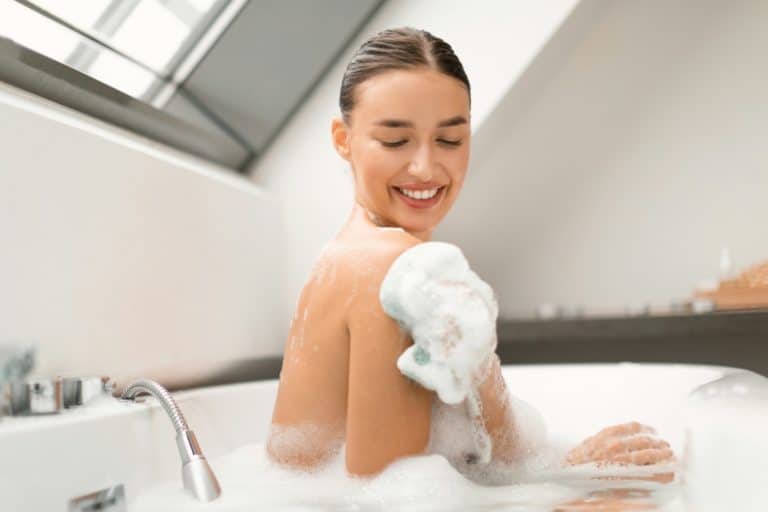 Happy Female Rubbing Body With Sponge Taking Bath At Home