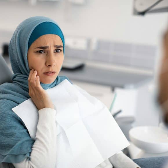 Teeth Problems. Muslim Female In Dentist Chair Showing Aching Tooth To Doctor