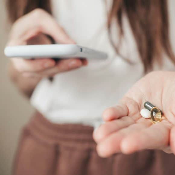 Vitamins for every day and a phone in the hands of the girl. spirulina, fish oil and magnesium